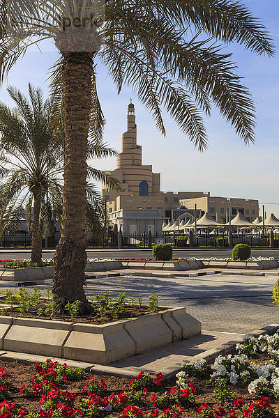 Palmen und Blumenbeete entlang der Uferpromenade Al-Corniche mit dem Islamischen Kulturzentrum Katar  Doha  Katar  Naher Osten