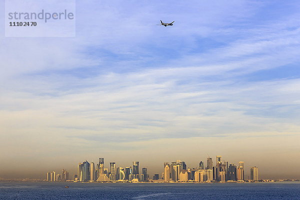 Düsenflugzeug nach dem Start vom internationalen Flughafen Hamad  vom Meer aus gesehen über der Skyline von Doha  Katar  Naher Osten