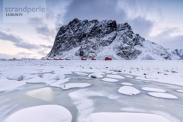 Schneegipfel und Eis umrahmen die typischen Fischerhäuser namens Rorbu  Eggum  Vestvagoy (Vest-Vagoy) Insel  Lofoten  Arktis  Norwegen  Skandinavien  Europa