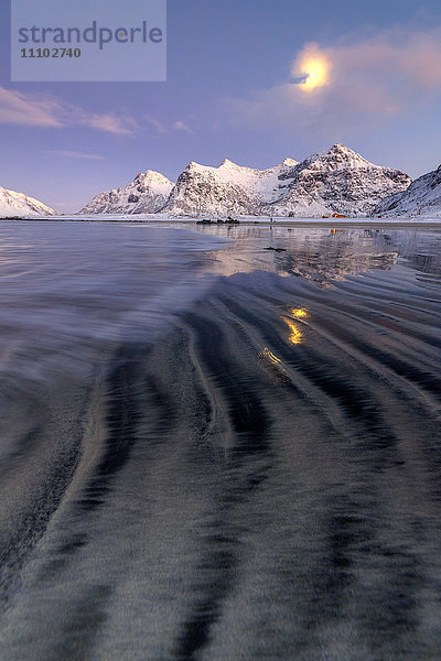 Der Vollmond spiegelt sich im eisigen Meer um den surrealen Skagsanden Strand  Flakstad  Nordland  Lofoten  Arktis  Norwegen  Skandinavien  Europa