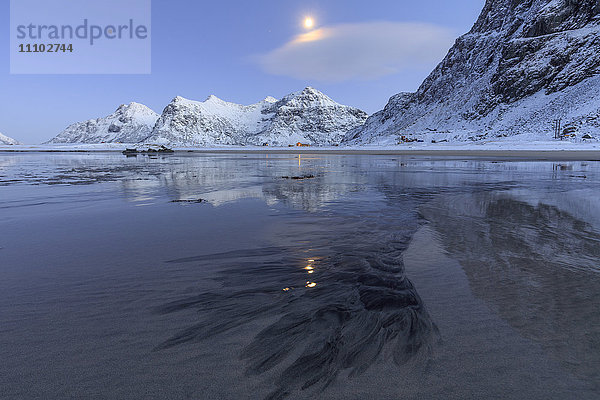 Der Vollmond spiegelt sich im eisigen Meer um den surrealen Skagsanden Strand  Flakstad  Nordland  Lofoten  Arktis  Norwegen  Skandinavien  Europa