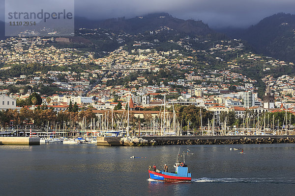 Funchal Stadt vom Meer mit Fischerboot  beleuchtet von der Abendsonne mit nebligem Berghintergrund  Funchal  Madeira  Atlantik  Portugal  Europa