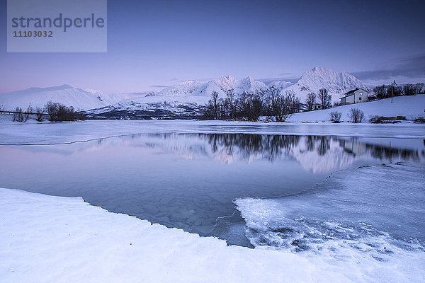 Schneebedeckte Gipfel spiegeln sich im gefrorenen See Jaegervatnet in der Abenddämmerung  Stortind  Lyngen Alps  Troms  Lappland  Norwegen  Skandinavien  Europa