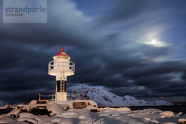 Leuchtturm und Vollmond in der arktischen Nacht mit dem Dorf Reine im Hintergrund  Nordland  Lofoten Inseln  Arktis  Norwegen  Skandinavien  Europa