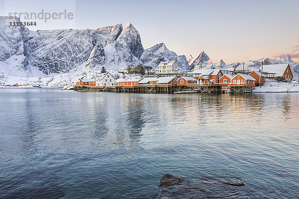 Die Farben der Morgendämmerung umrahmen die von verschneiten Gipfeln umgebenen Fischerhäuser  Sakrisoy  Reine  Nordland  Lofoten  Arktis  Norwegen  Skandinavien  Europa