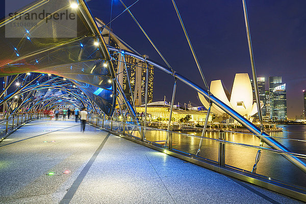 Menschen schlendern auf der Helix-Brücke in Richtung Marina Bay Sands und ArtScience Museum bei Nacht  Marina Bay  Singapur  Südostasien  Asien