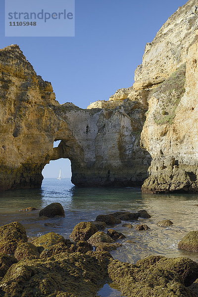 Verwitterte Sandsteinklippen und Schornsteine bei Ponta da Piedade im Morgenlicht mit einer von einem Felsbogen eingerahmten Jacht  Lagos  Algarve  Portugal  Europa
