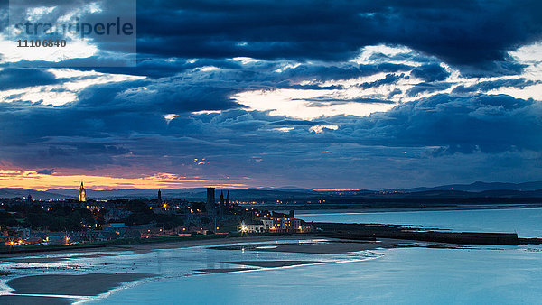 Blick über die Bucht auf den Hafen und den Pier von St. Andrews  während die Sonne in der Abenddämmerung hinter der Stadt untergeht  St. Andrews  Fife  Schottland  Vereinigtes Königreich  Europa