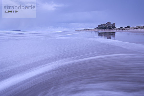 Wellen spülen über den Strand neben Bamburgh Castle an einem stürmischen Winterabend  Northumberland  England  Vereinigtes Königreich  Europa