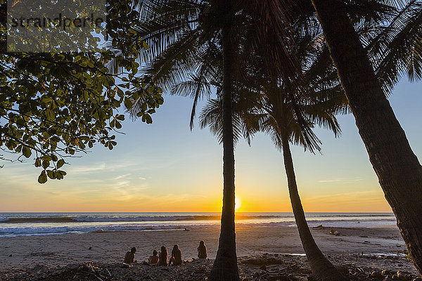 Menschen unter Palmen bei Sonnenuntergang am Strand Playa Hermosa  ganz im Süden der Nicoya-Halbinsel  Santa Teresa  Puntarenas  Costa Rica  Mittelamerika