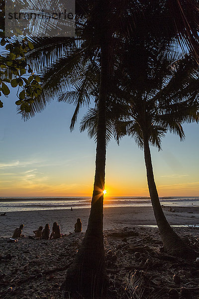 Menschen unter Palmen bei Sonnenuntergang am Strand Playa Hermosa  ganz im Süden der Nicoya-Halbinsel  Santa Teresa  Puntarenas  Costa Rica  Mittelamerika