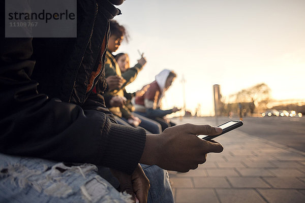 Mittelteil des Teenagers beim Telefonieren mit Freunden in der Kopfsteinpflasterstraße