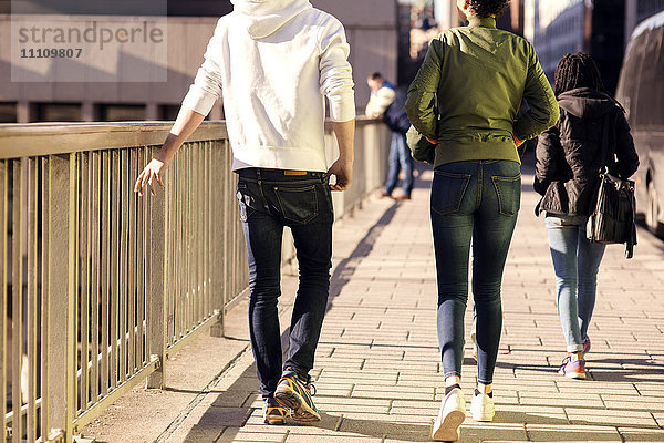 Rückansicht von Freunden  die auf der Brücke mit dem Geländer in der Stadt spazieren gehen.