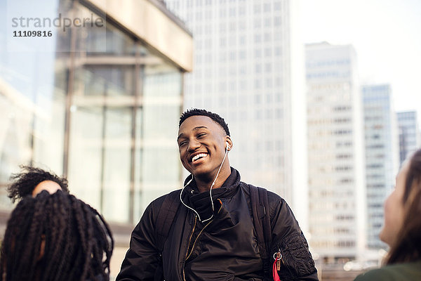 Lächelnder Teenager mit Kopfhörer im Stehen mit Freunden in der Stadt