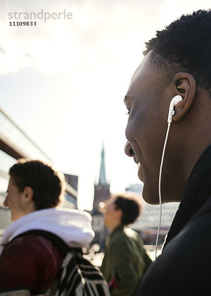 Abgeschnittenes Bild eines Teenagers  der Musik hört  während er mit Freunden gegen den Himmel geht.
