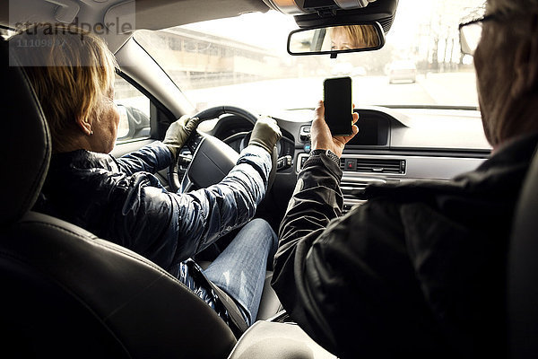 Senior Frau  die Auto fährt  während sie von Mann zu Mann sitzt und Selfie über Smartphone nimmt.
