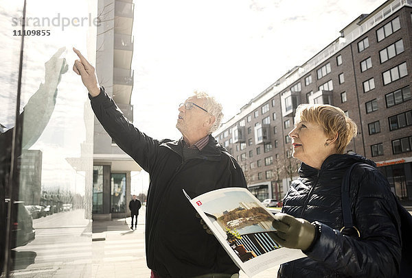 Seniorin liest Katalog  während der Mann auf ein Glasfenster in der Stadt zeigt.