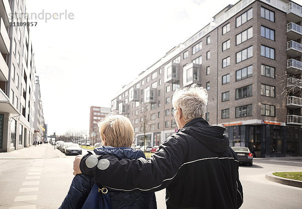 Rückansicht des Seniorenpaares  das auf der Stadtstraße gegen den klaren Himmel geht.