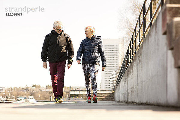 Seniorenpaar in Sportbekleidung beim Gehen auf dem Bürgersteig gegen den klaren Himmel