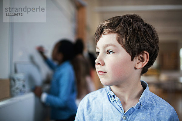 Nahaufnahme eines männlichen Schülers  der im Klassenzimmer steht und wegschaut.