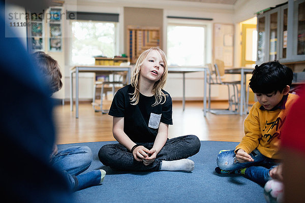 Mädchen im Gespräch mit Freunden auf dem Boden im Klassenzimmer