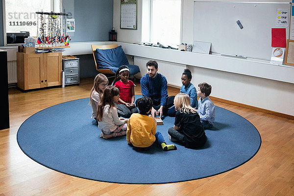 Lehrer  der mit Schülern spielt  während er in der Schule auf dem Boden sitzt.