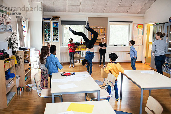 Schüler  die einen männlichen Lehrer beim Handstand im Klassenzimmer beobachten.