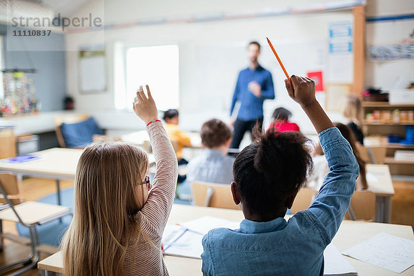 Rückansicht der Schüler mit erhobenen Händen im Klassenzimmer