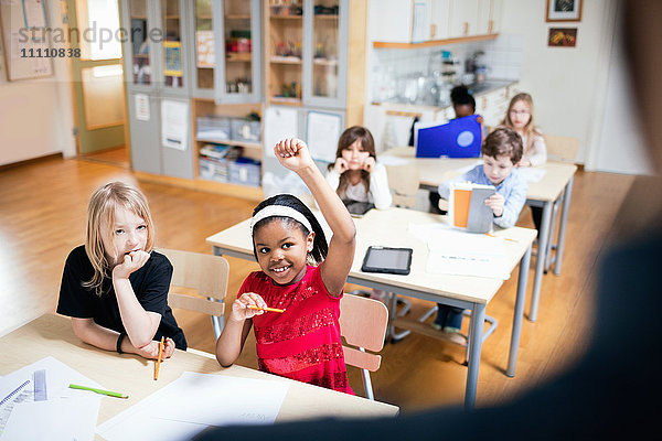 Lächelnder Schüler mit erhobener Hand im Klassenzimmer sitzend