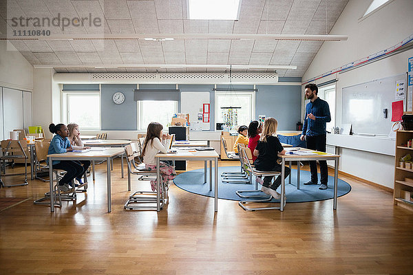 Lehrer  der die Schüler in einem hell erleuchteten Klassenzimmer unterrichtet.