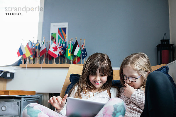 Lächelnde Freunde beim Sitzen auf dem Sofa in der Schule mit dem digitalen Tablett