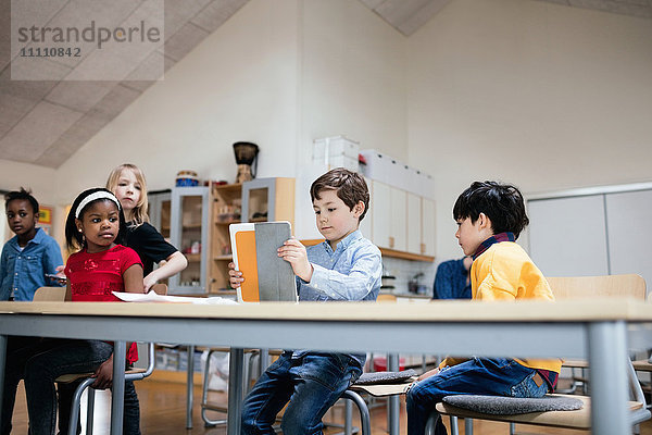 Schüler  die den Jungen mit dem digitalen Tablett im Klassenzimmer in der Schule betrachten