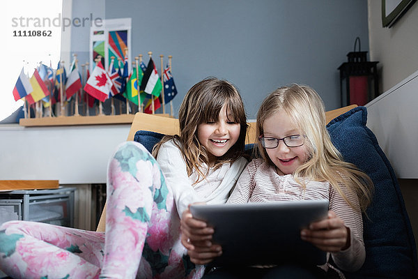 Lächelnde Freunde  die in der Schule auf dem Sofa liegen und ein digitales Tablett benutzen.