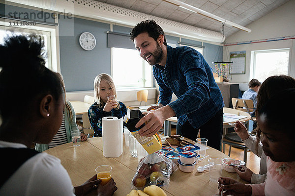 Lehrer serviert Saft für Schüler  die am Tisch im Klassenzimmer sitzen.