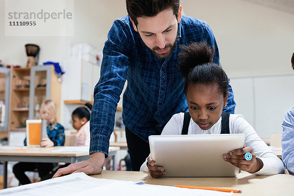 Lehrerin beim Betrachten eines Mädchens mit digitalem Tablett im Klassenzimmer