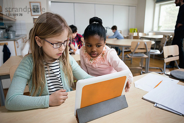 Seriöse Schüler  die im Klassenzimmer sitzen und sich das digitale Tablett anschauen.