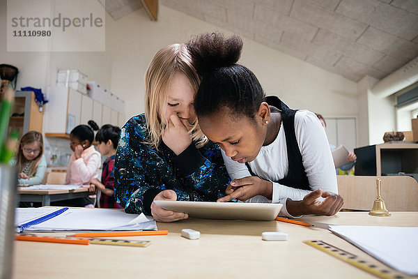 Multi-ethnische Schüler mit digitalem Tablett am Schreibtisch im Klassenzimmer