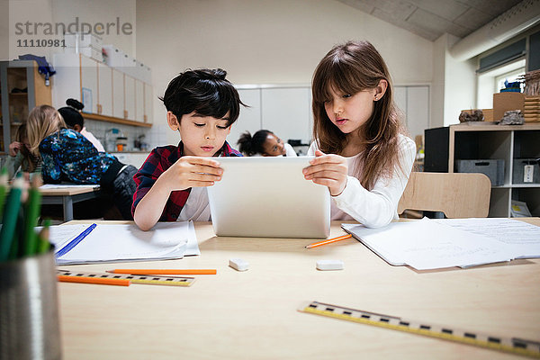 Konzentrierte Schüler mit digitalem Tablett am Schreibtisch im Klassenzimmer