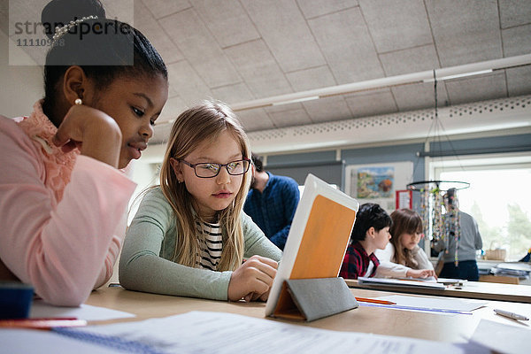 Schülerinnen lesen digitales Tablett am Schreibtisch im Klassenzimmer