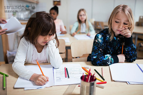 Schüler schreiben auf Papier am Schreibtisch im Klassenzimmer