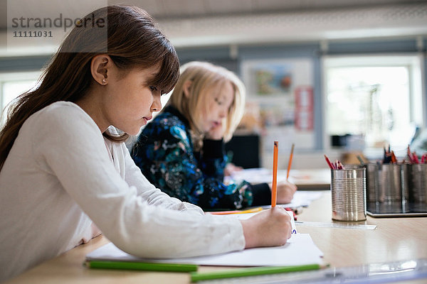 Seitenansicht der Schüler beim Schreiben auf Papier am Schreibtisch im Klassenzimmer