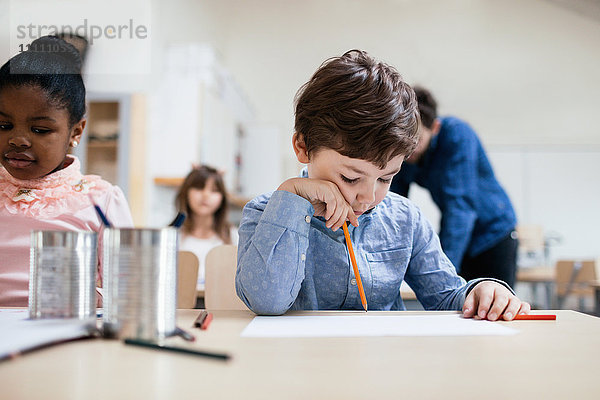 Ernsthafter Junge studiert  während der Lehrer im Hintergrund in der Schule steht.