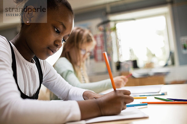 Konzentriertes Schreiben von Mädchen am Schreibtisch im Klassenzimmer