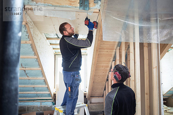 Mitarbeiter bei der Schreinerbohrung am Dachbalken auf der Baustelle