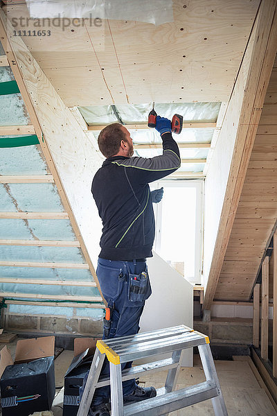 Mann bohrt Holzbohlen auf Dachbalken im Haus