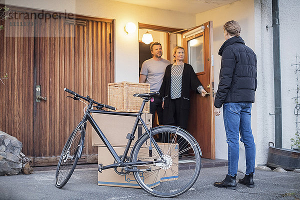 Mann  der die Eltern im Stehen mit Pappkartons und Fahrrad am Hauseingang ansieht.