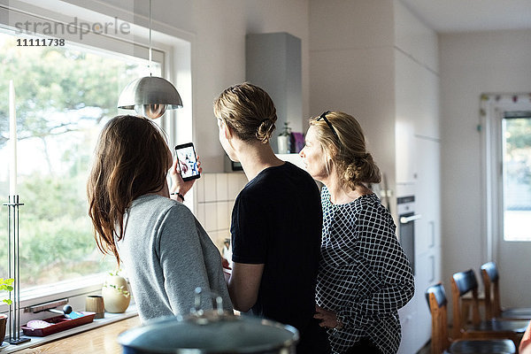 Frau nimmt Selfie  während sie mit der Familie in der Küche im neuen Zuhause steht