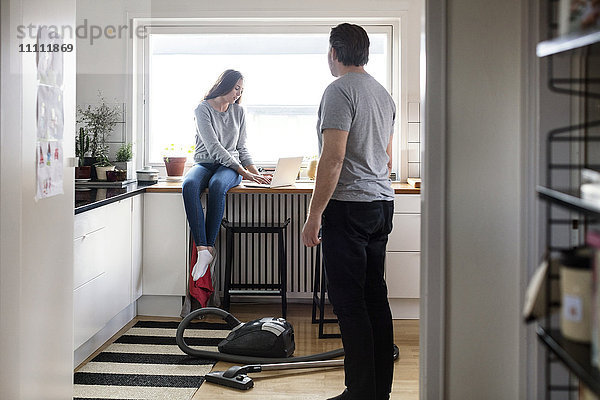 Vater schaut auf Tochter mit Laptop auf Küchenarbeitsplatte im neuen Haus