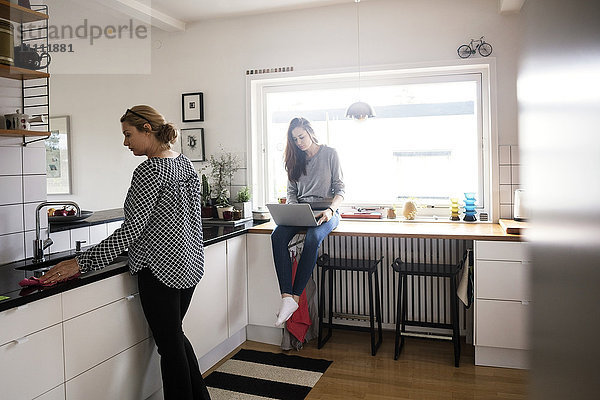 Mutter arbeitet  während Tochter mit Laptop in der Küche in der neuen Heimat