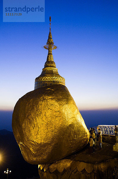 Asien  Myanmar  Kyaiktiyo ist ein Ort der ersten Pilgerfahrt zur buddhistischen Religion. Es wird angenommen  dass die sieben Buddha-Hüte  die sich in der obersten Stupa befinden  in perfektem Gleichgewicht zueinander stehen. Der Felsblock ist buchstäblich mit Gold bedeckt  da die Pilger bei Sonnenuntergang Blattgold auf den Felsen streuen.
